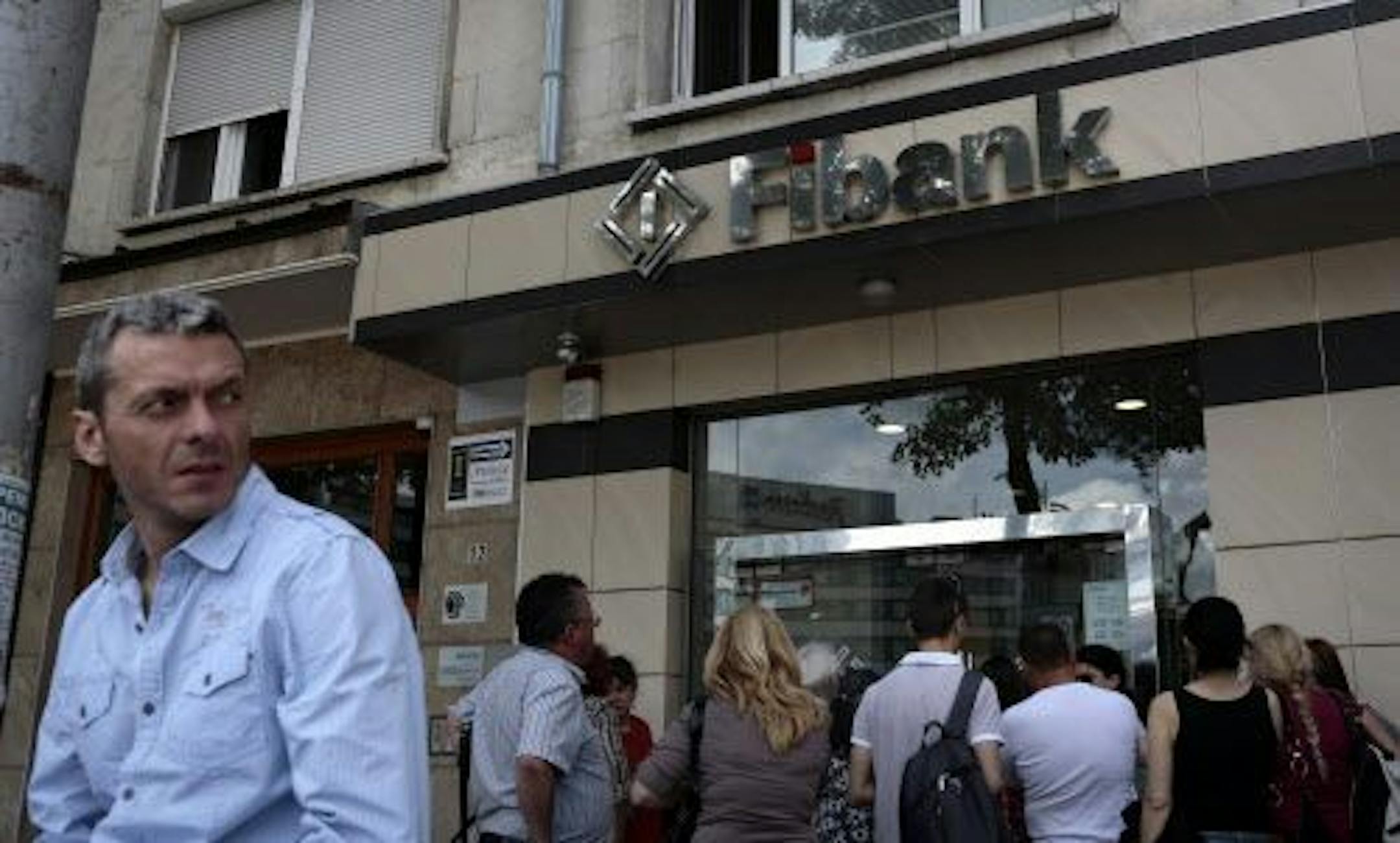 A man stands in front of a branch of First Investment Bank as people wait outside after closing time, Sofia, Friday, June 27, 2014.