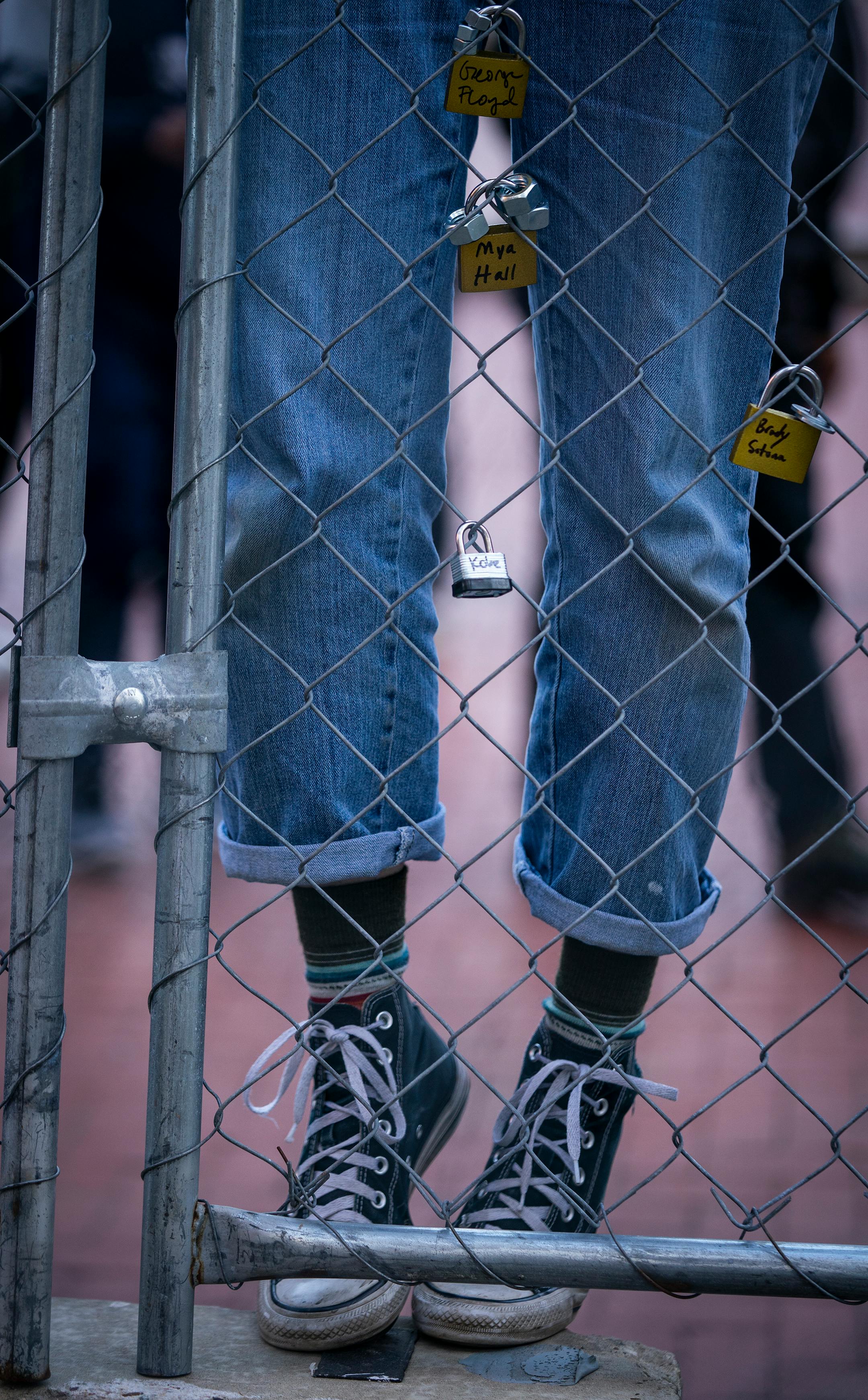 A person stands on the barricade on their toes to reach and place a lock on the fence outside the Hennepin County Government Center during the Locks for Loved Ones Lost: Part II event.