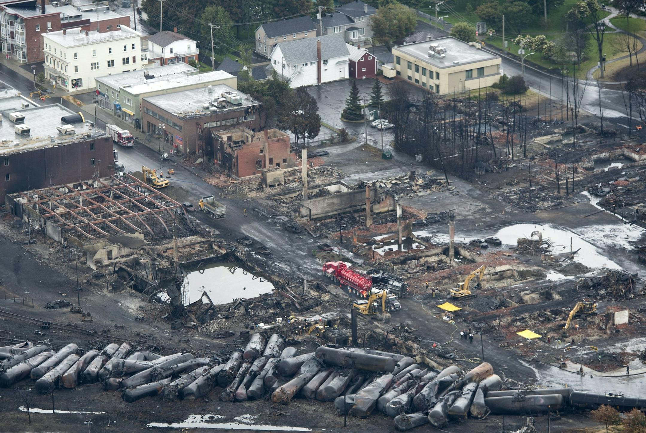 This aerial photo, workers comb through the debris after a train derailed causing explosions of railway cars carrying crude oil Tuesday, July 9, 2013 in Lac-Megantic, Quebec, Canada on Tuesday July 9, 2013. At least thirteen people were confirmed dead and nearly 40 others were still missing in a catastrophe that raised questions about the safety of transporting oil by rail instead of pipeline. (AP Photo/ The Canadian Press, Paul Chiasson)