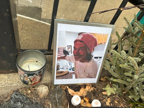 A memorial to Robert Skafte outside Oak Grove Grocery in Minneapolis shown in close detail with a photo, candle and flowers.