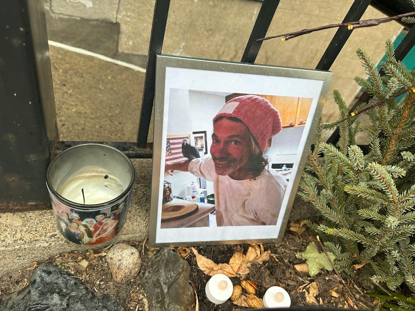 A memorial to Robert Skafte outside Oak Grove Grocery in Minneapolis shown in close detail with a photo, candle and flowers.