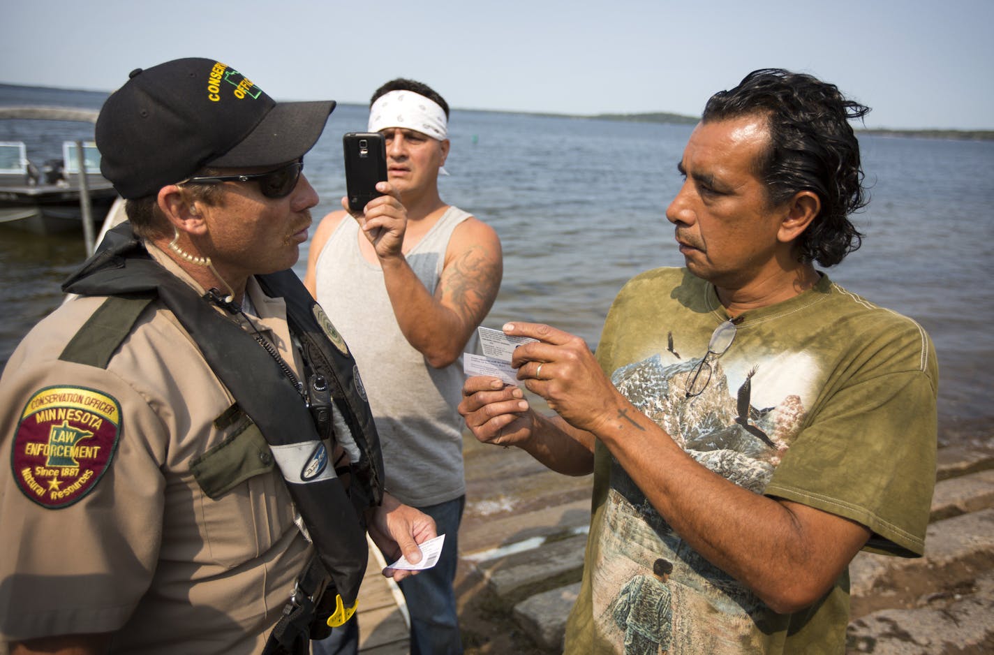 DNR conservation officer Tim Collette gives a citation to Jim Northrup (right) and Todd Thompson, (with phone) for Taking Fish by Illegal Methods for setting a gill net on Gull Lake Friday morning. ] Two tribal members who attempted to net fish on Gull Lake Friday were chased off the lake and given citations by state conservation officers who then pulled the 200-foot long net from the water and carried it away. Brian.Peterson@startribune.com Nisswa, MN - 8/27/2015