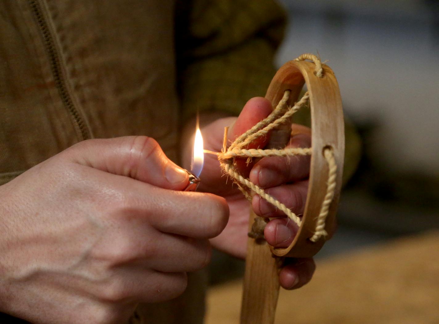 Maxwell Kelsey used fire to singe a knot on a lacrosse stick netting. He had earlier in the morning made the netting from twisted wood fibers soaked in water to soften them.