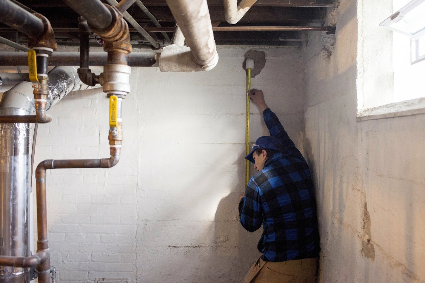 Drew Gardner of Drew Gardner Concrete and Waterproofing measures the height of the wall to determine how long the pipe needs to be. The pipe will exit the home, and discharge water outside when it is collected.