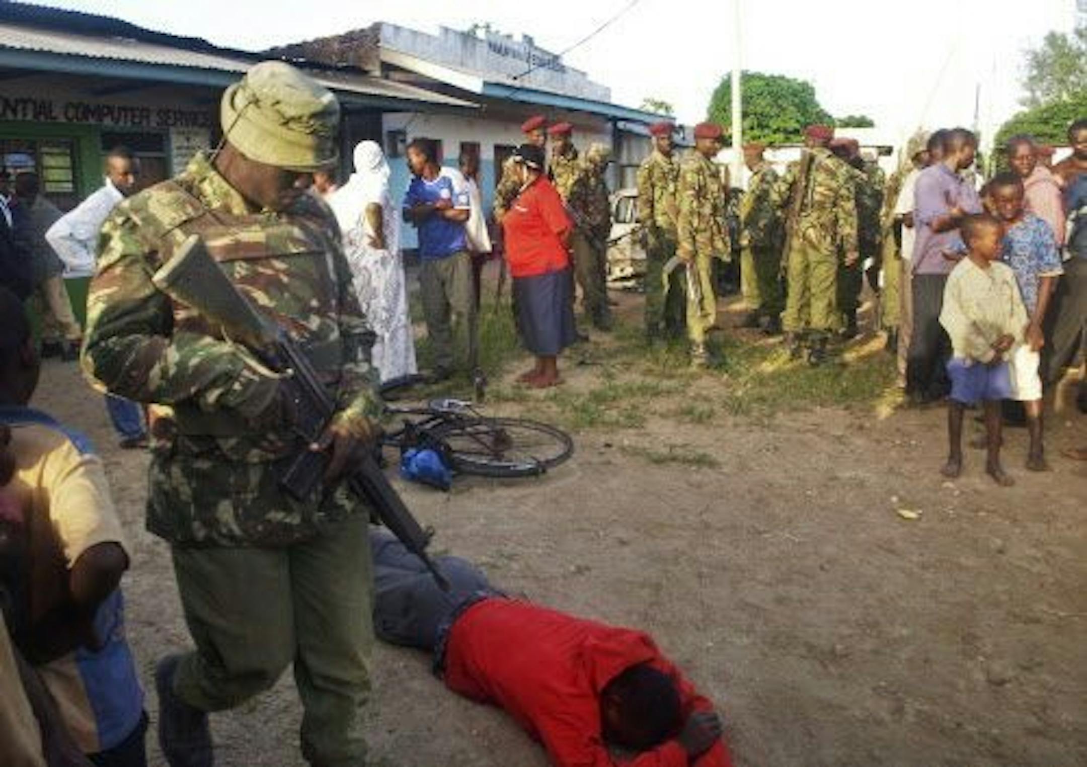 A member of the Kenyan security forces walks past the body of one of those who were killed by militants, in the village of Kibaoni, Monday, June 16, 2014.