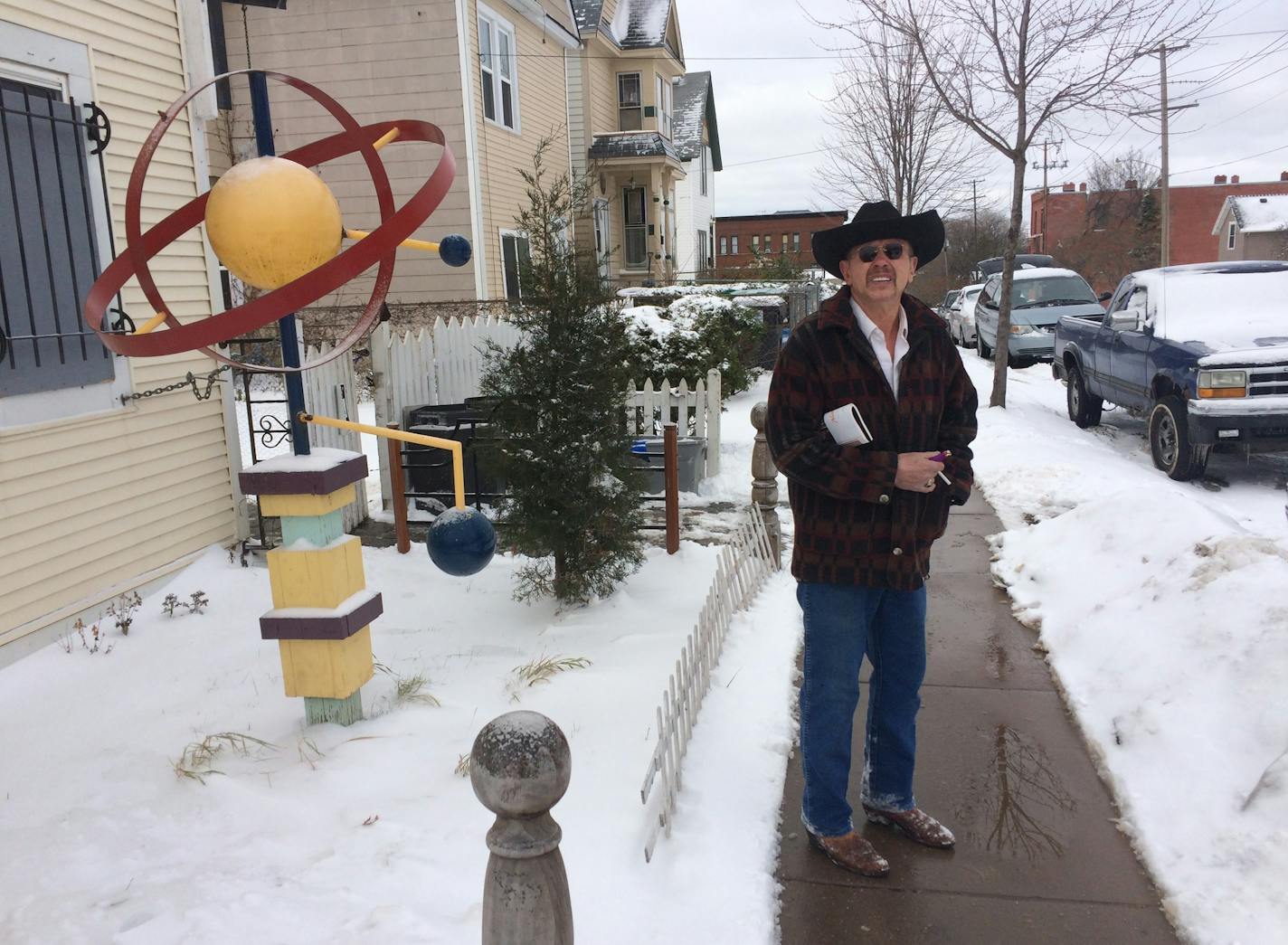 Arjo Adams stands in front of his house, with one of his yard sculptures. He has to use a back door, because the city boarded the front door when it declared the house vacant.