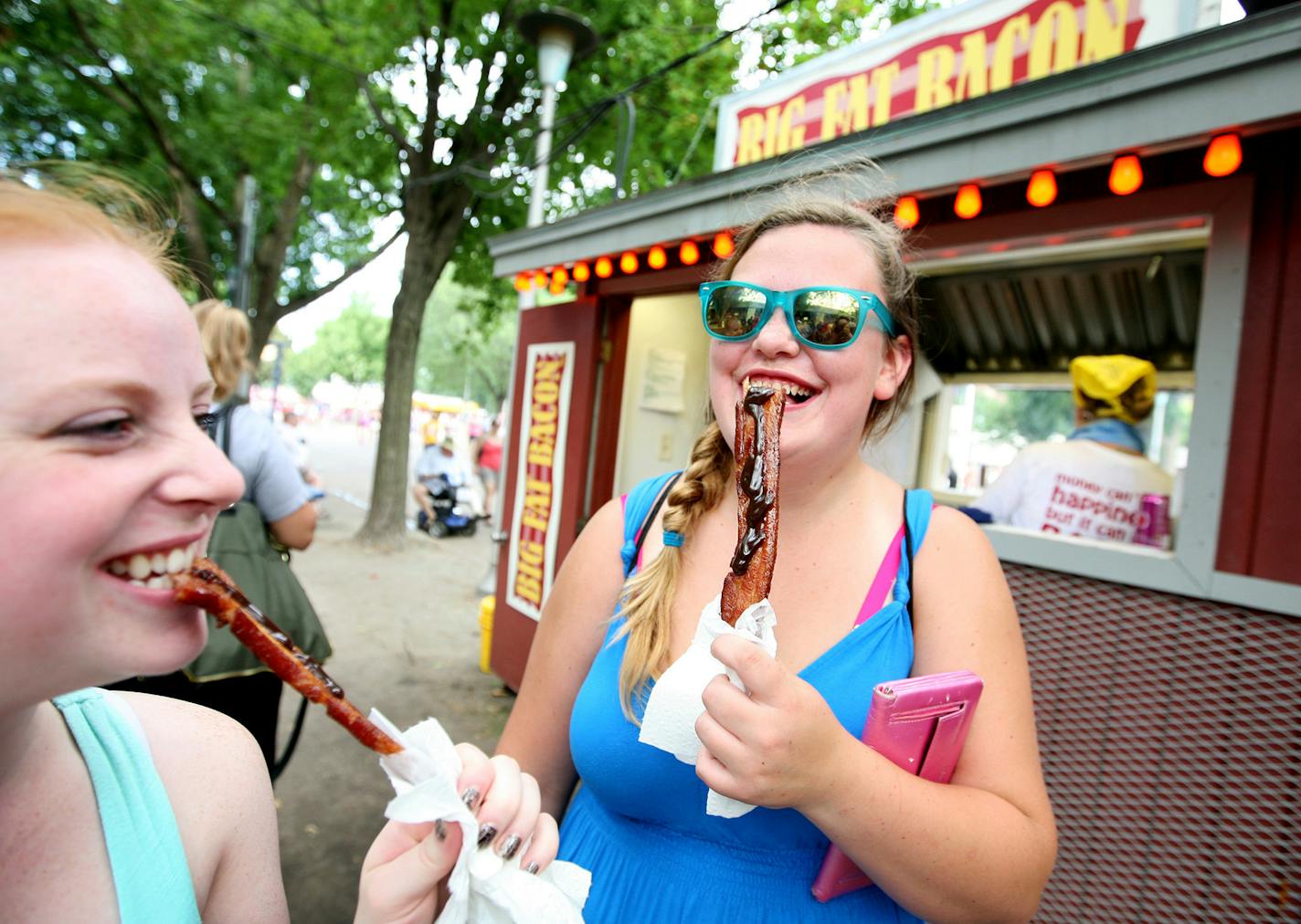 Sisters Britney Payne, left, of Inver Grove Heights and Alexis Geving of Ogilvie enjoy bacon with drizzled chocolate from Big Fat Bacon at the Minnesota State Fair Aug. 25, 2013.