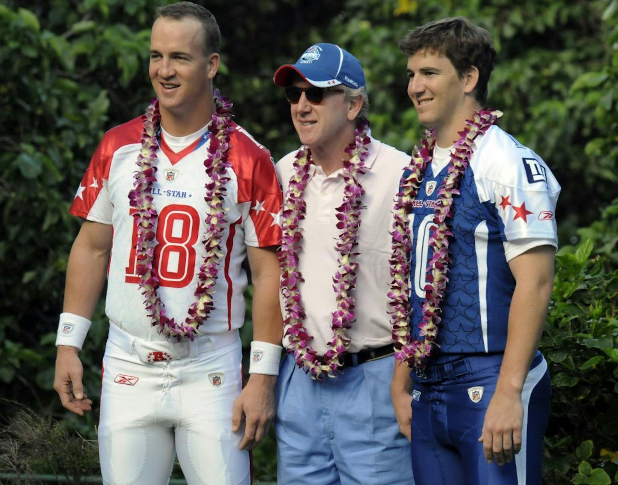 In this Feb. 6, 2009, file photo, Indianapolis Colts quarterback Peyton Manning, left, and New York Giants quarterback Eli Manning, right, pose for photos with their dad Archie Manning, center, before Pro Bowl practice