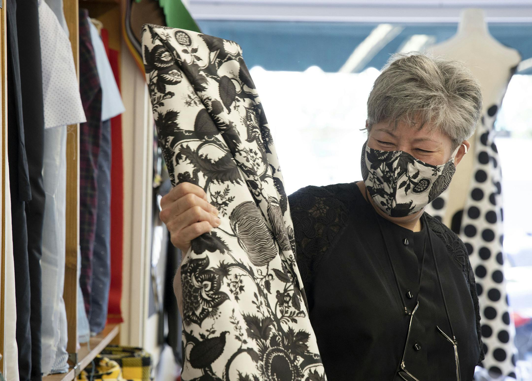 Tami Sampson, owner of The Fabric Place, holds up a bolt of Italian cotton fabric that matches her mask in her shop on July 28, 2020 in Mt. Lebanon, Pa. Ms. Sampson's store, which sells only clothing fabric, has been receiving customers new to sewing who are learning to make masks during the pandemic. (Lily LaRegina/Pittsburgh Post-Gazette/TNS) ORG XMIT: 1755215
