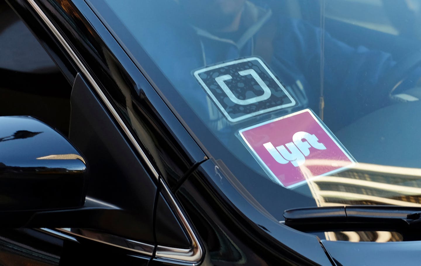 A ride share car displays Lyft and Uber stickers on its front windshield