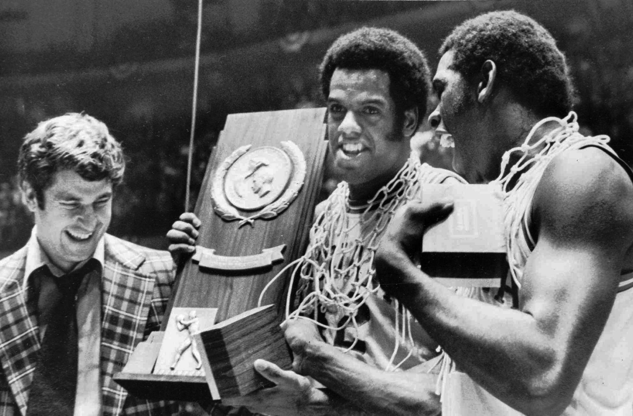 University of Indiana coach Bobby Knight (at left) and team members Scott May (center) and Quinn Buckner (right) are all smiles as they hold the trophy for winning the NCAA Basketball championship in Philadelphia, Monday night, March 30, 1976. (Associated Press Photo)