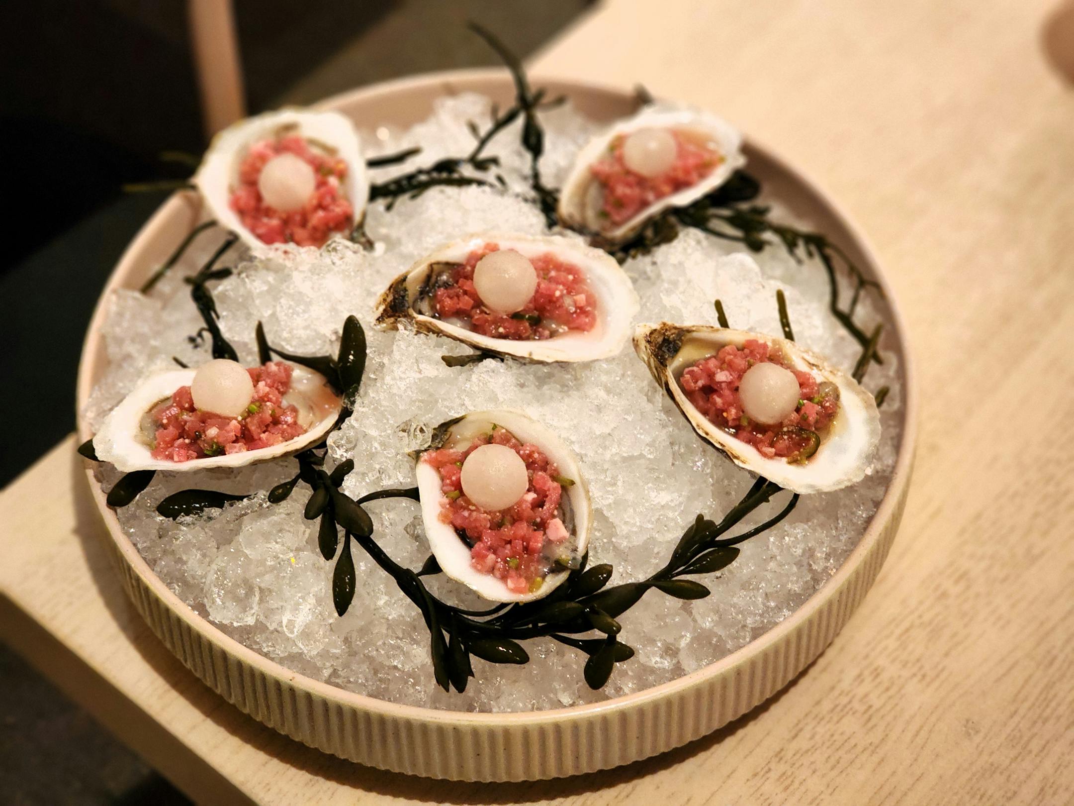 A platter with oysters topped with pink chopped beef and little white spheres of frozen lime