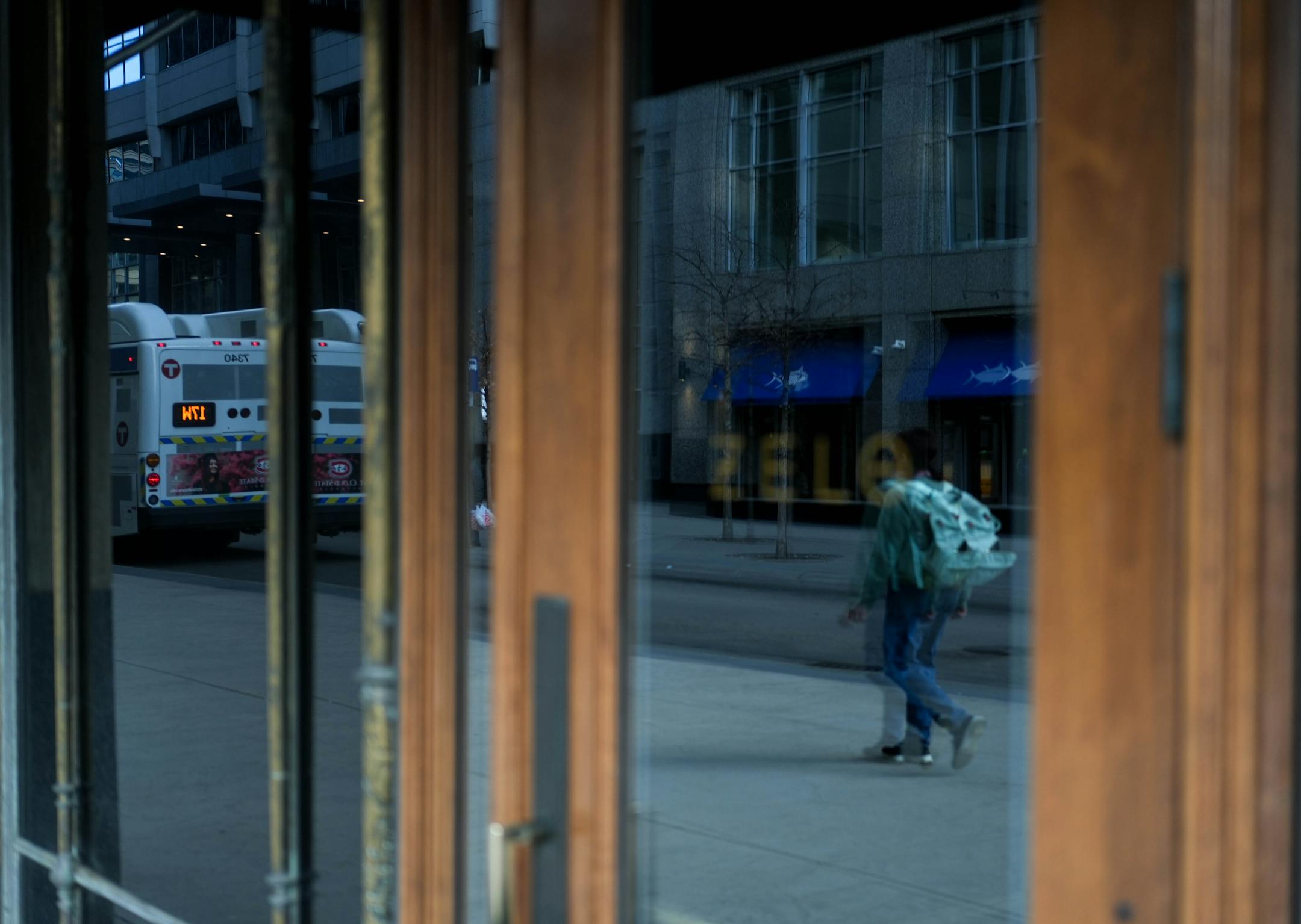 A restaurant's heavily tinted facade reflects a street with a pedestrian and a city bus passing by.
