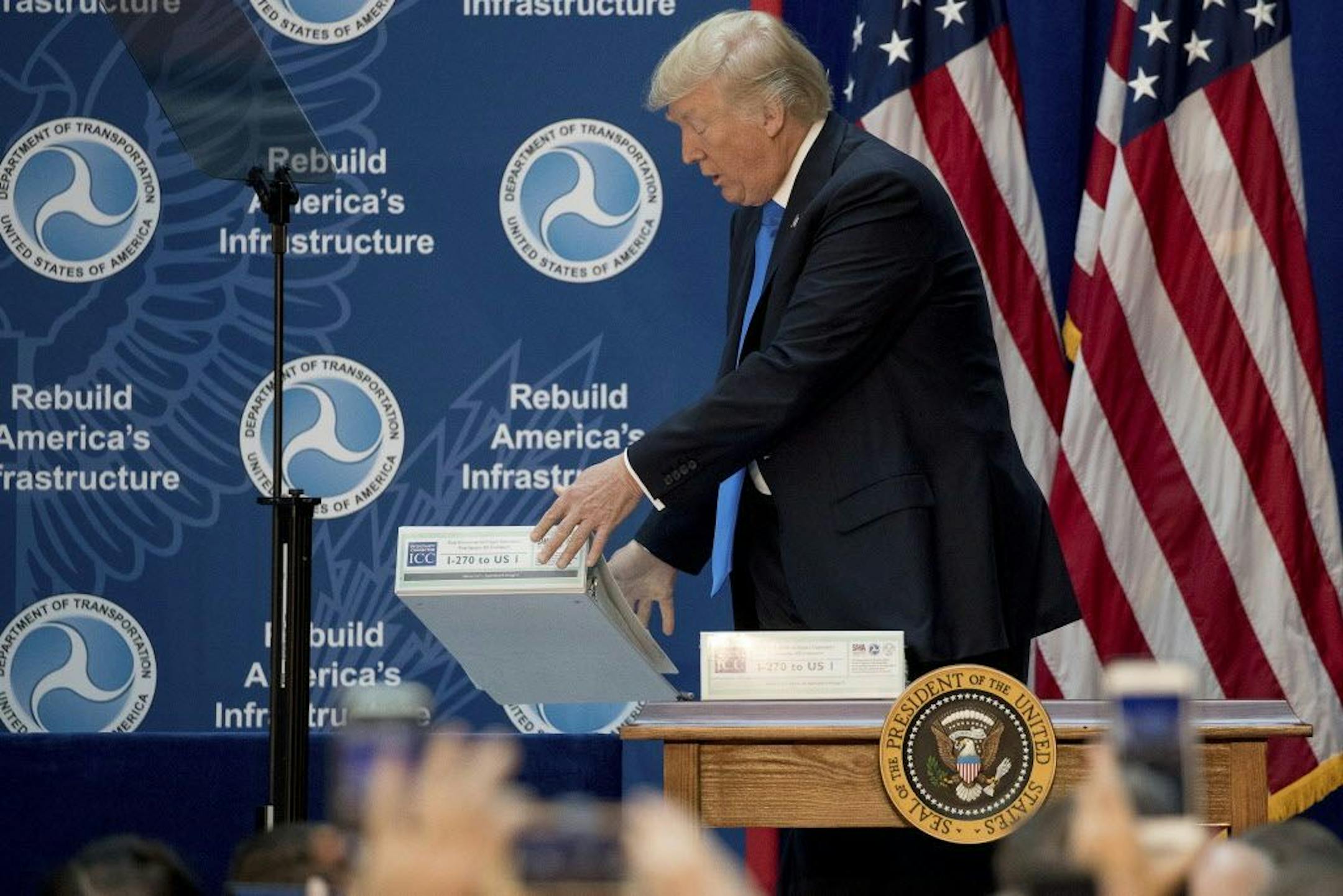President Donald Trump drops environmental impact statements for a highway plan in Maryland on the ground while speaking on infrastructure at the Department of Transportation, Friday, June 9, 2017, in Washington.