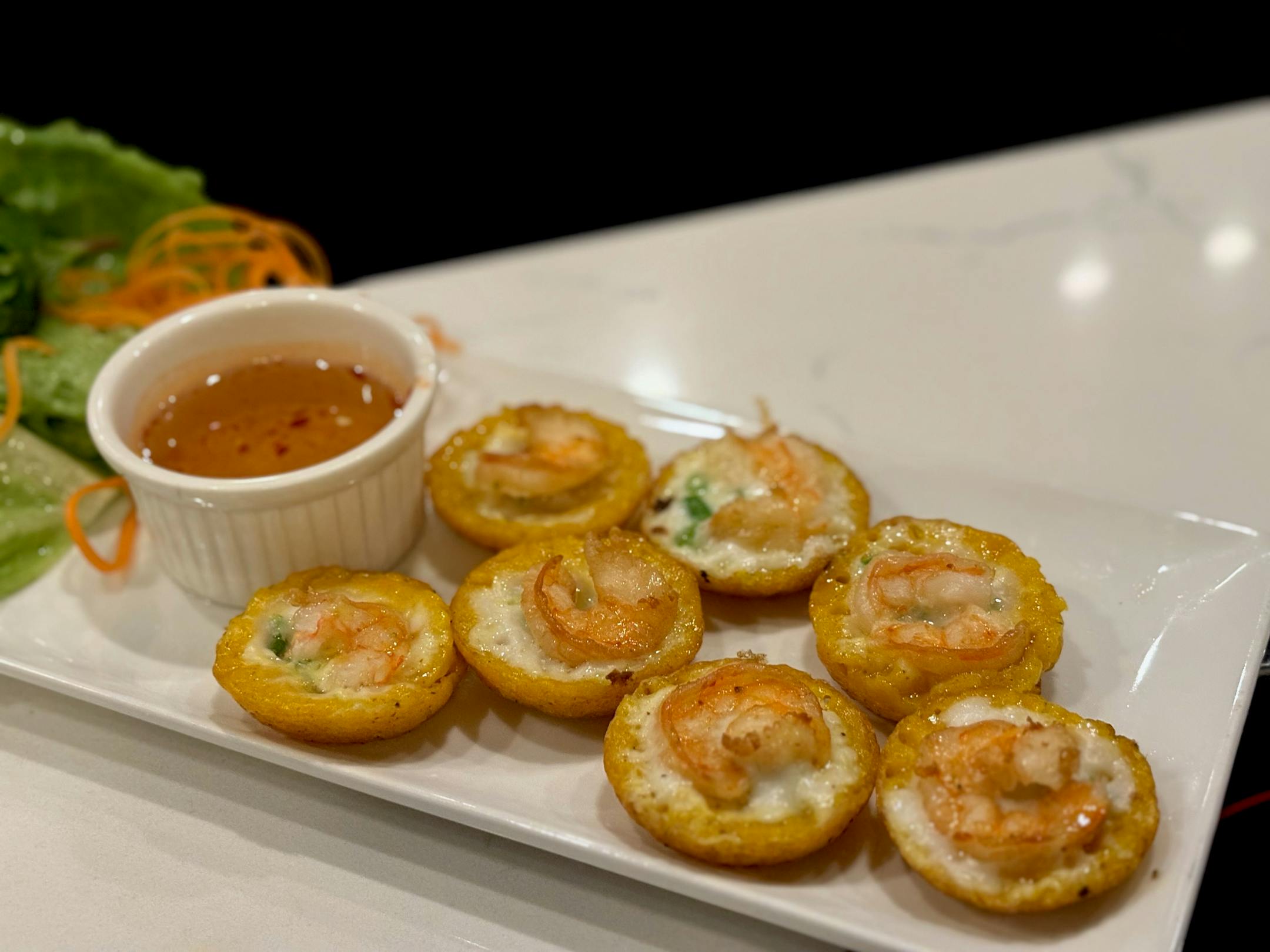 7 banh khot on a white platter with nước chấm and lettuce leaves.