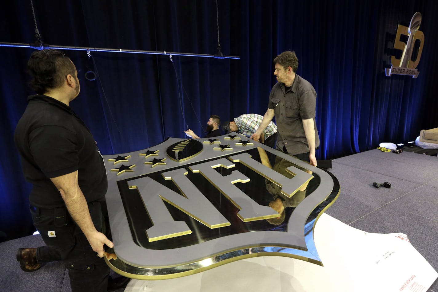 Workers hang an NFL shield on the main stage before a news conference Thursday, Feb. 4, 2016, in San Francisco. (AP Photo/David J. Phillip)