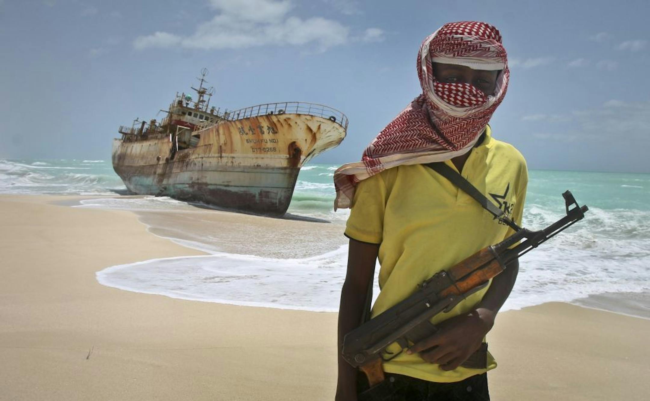 FILE - In this Sunday, Sept. 23, 2012 file photo, masked Somali pirate Hassan stands near a Taiwanese fishing vessel that washed up on shore after the pirates were paid a ransom and released the crew, in the once-bustling pirate den of Hobyo, Somalia. Frustrated by a string of failed hijacking attempts, Somali pirates have turned to a new business model: transporting weapons and providing "security" for ships illegally plundering Somalia's fish stocks - the same scourge that launched the Horn of