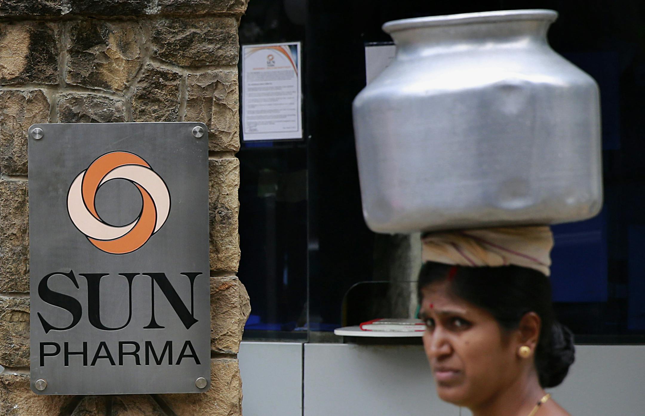 An Indian woman carries a water vessel as she walks past the office of Sun Pharmaceutical in Mumbai, India, Monday, April 7, 2014. The Sun Pharmaceutical Industries is buying troubled generic drugmaker Ranbaxy Laboratories in a $4 billion all-stock transaction, the companies said Monday. (AP Photo/Rafiq Maqbool)