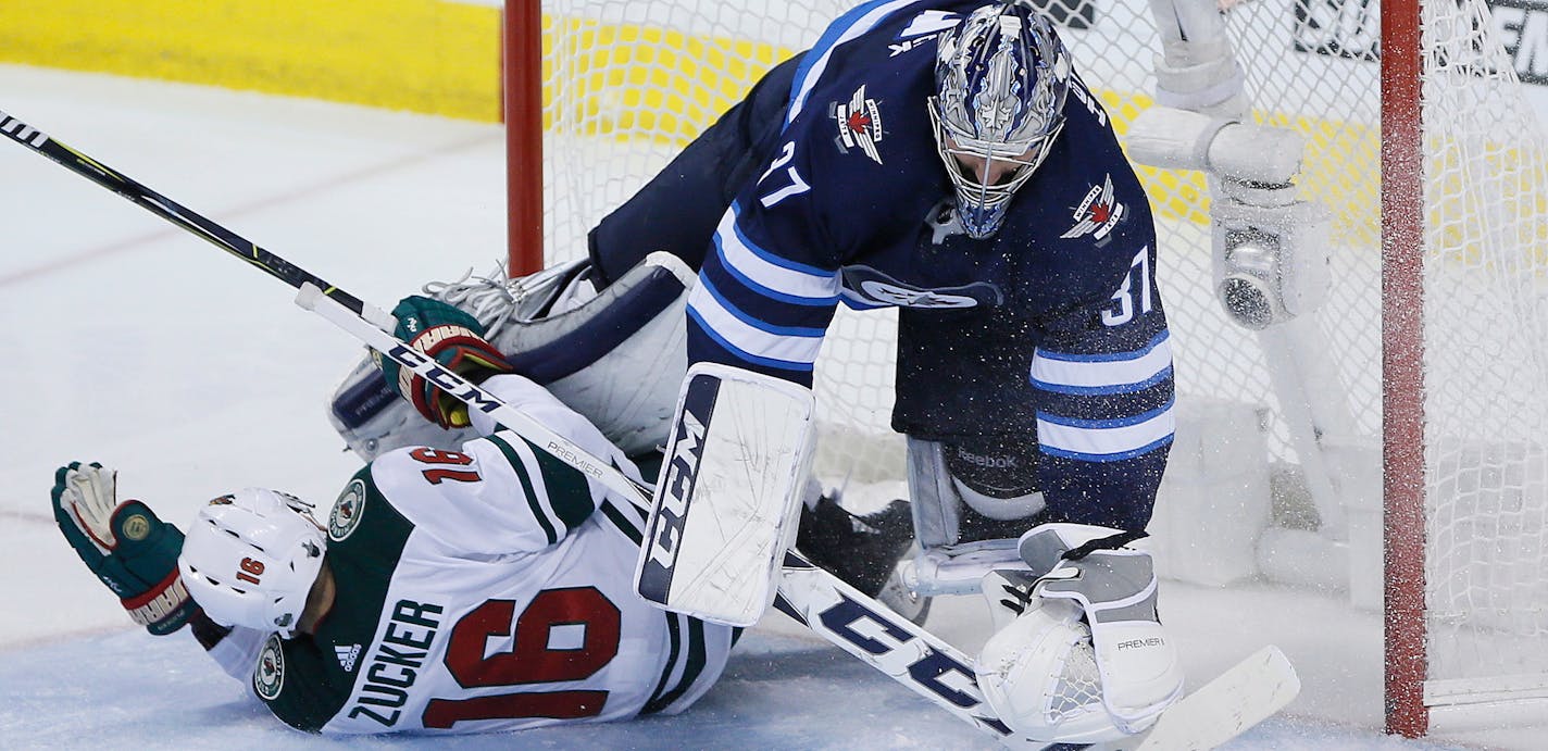 Winnipeg Jets goaltender Connor Hellebuyck (37) gets taken down by Minnesota Wild's Jason Zucker (16) during the third period in Game 5 of an NHL hockey first-round playoff series in Winnipeg, Manitoba, Friday, April 20, 2018. (John Woods/The Canadian Press via AP)