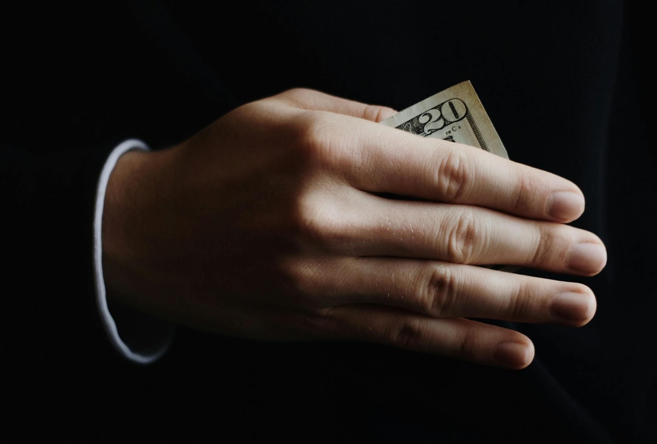 A single hand holding out money as a bribe