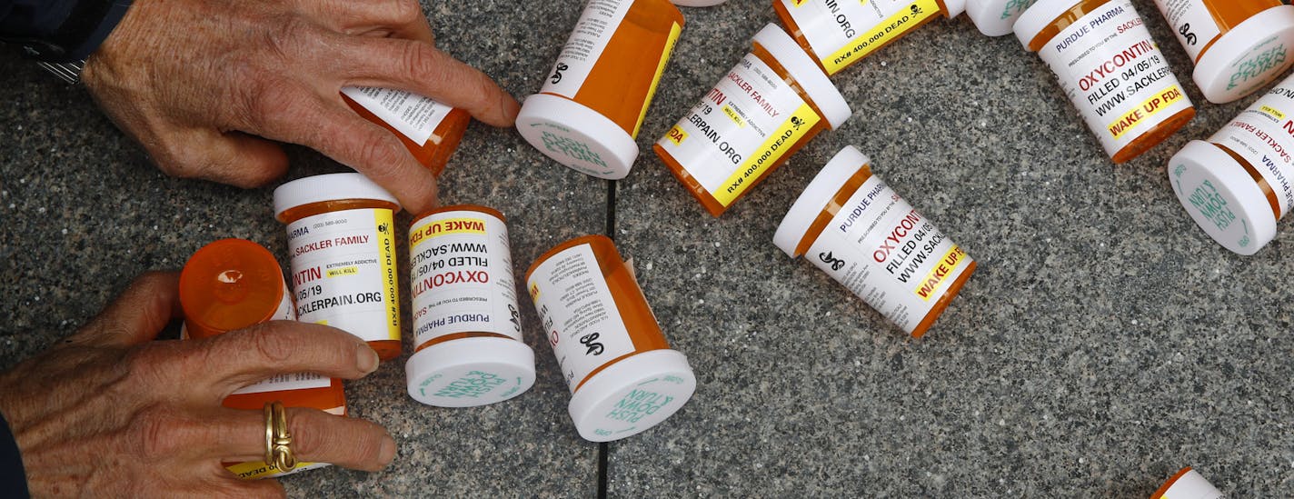 FILE - In this Friday, April 5, 2019, file photo, a protester gathers containers that look like OxyContin bottles at an anti-opioid demonstration in front of the U.S. Department of Health and Human Services headquarters in Washington, D.C. The U.S. has backed away from recommending opioids for long-term treatment of chronic pain. Nevertheless, companies continue pushing the drugs in other countries, and consumption is growing. Researchers in Brazil report, for example, that prescription opioid s