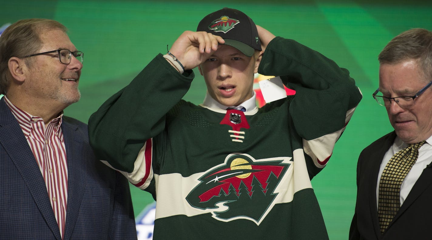 Matthew Boldy puts on a Minnesota Wild hat after being chosen by the team during the first round of the NHL hockey draft Friday, June 21, 2019, in Vancouver, British Columbia. (Jonathan Hayward/The Canadian Press via AP)