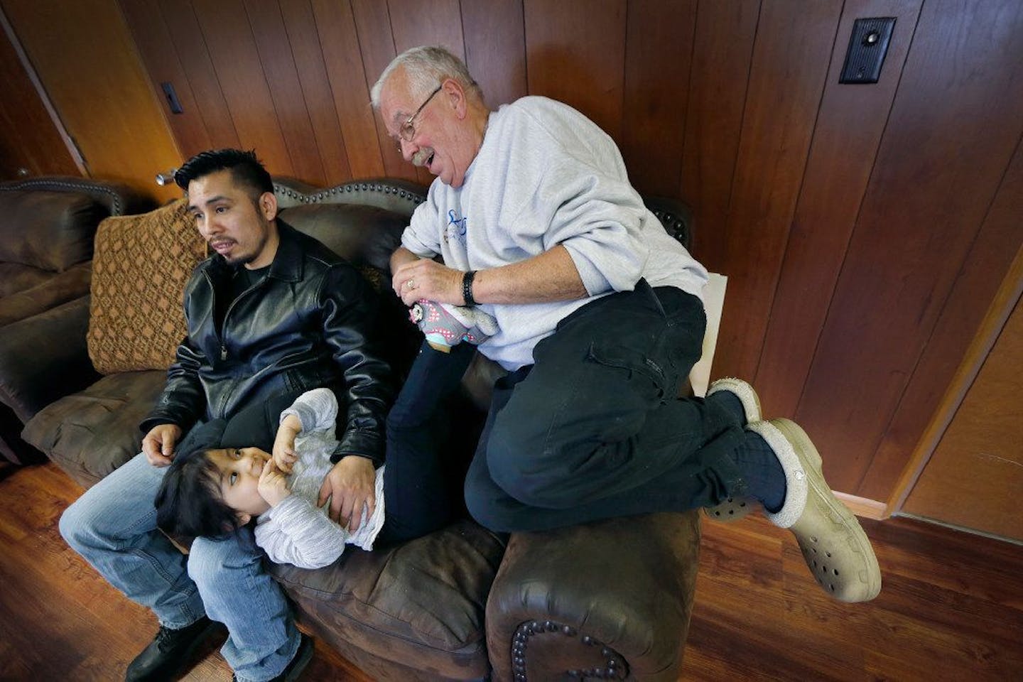 Father Jim Callahan, right, of St. Mary's Catholic Church played with Maria, 2, who relaxed with her father Enrique at the church in February 2017 in Worthington, MN. Enrique and his family lost their home and all of their belongings to a fire and came to live with Father Callahan.