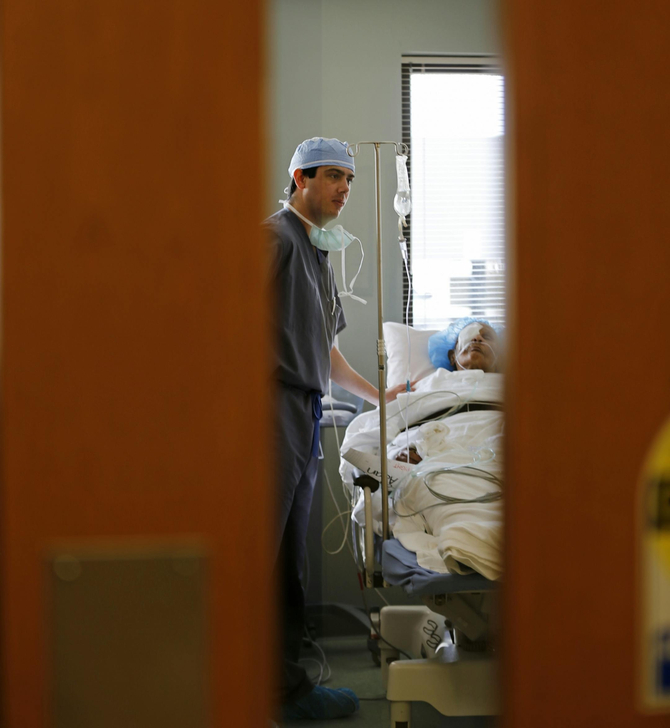 Dr. Walter Parker could be seen through a door as he checked on a patient in a post-operation space after removing a cataract from the patient's right eye.
