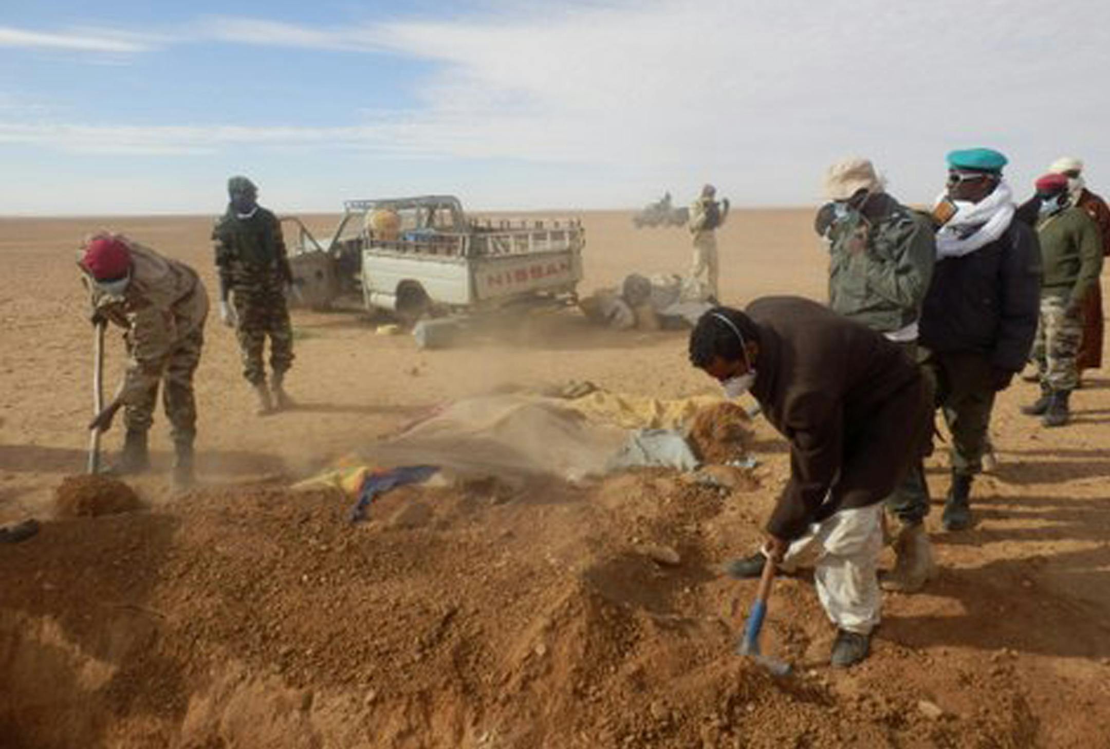 In this Wednesday, Oct. 30, 2013 photo, volunteers and officials dig graves to inter the bodies of migrants who died of thirst after their the truck they were traveling in, seen rear, broke down while attempting to cross the Sahara Desert north of Arlit, Niger. Nearly 100 African migrants hoping to escape crushing poverty met a grisly end in the desert, officials said Thursday, dying of thirst under the baking sun after their truck broke down in Niger not far from the Algerian border. It took we