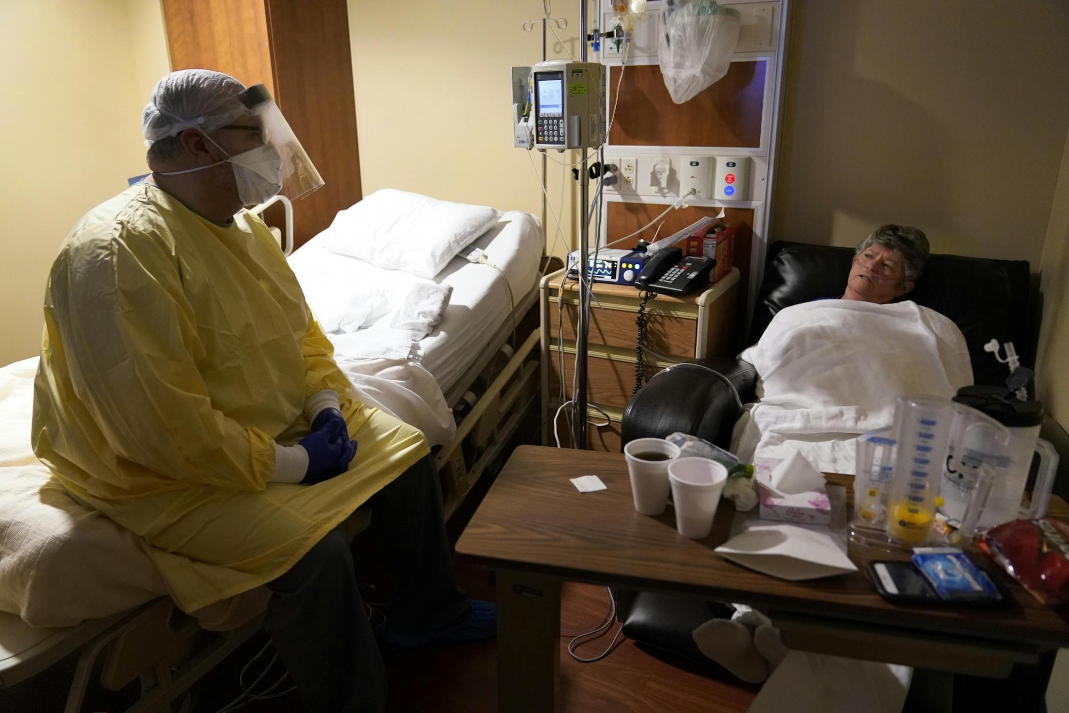 Dr. Shane Wilson, left, sits on a bed as he talks with COVID-19 patient JoBeth Harvey while performing rounds in a portion of Scotland County Hospital set up to isolate and treat COVID-19 cases on Tuesday, Nov. 24, 2020, in Memphis, Mo. Harvey used to be a gym teacher at Wilson's school and laughingly recalls a day she caught him smoking. She made him and a friend pick up cigarette butts as punishment.