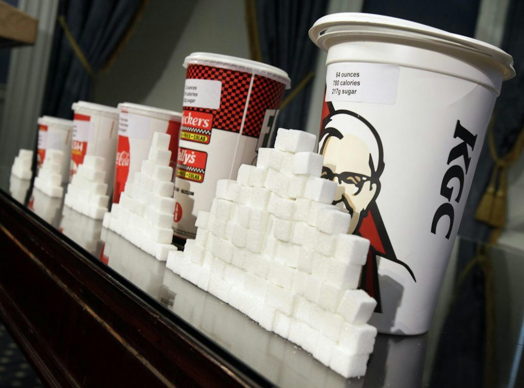 FILE - This Thursday, May 31, 2012 file photo shows a display of various size soft drink cups next to stacks of sugar cubes at a news conference at New York's City Hall. New research greatly strengthens the case against soda and other sugary drinks as culprits in the obesity epidemic. Two major experiments found that children and teens gained less weight when they regularly drank calorie-free beverages instead of sugary ones. A third study gives the first clear evidence that consuming sugary dri