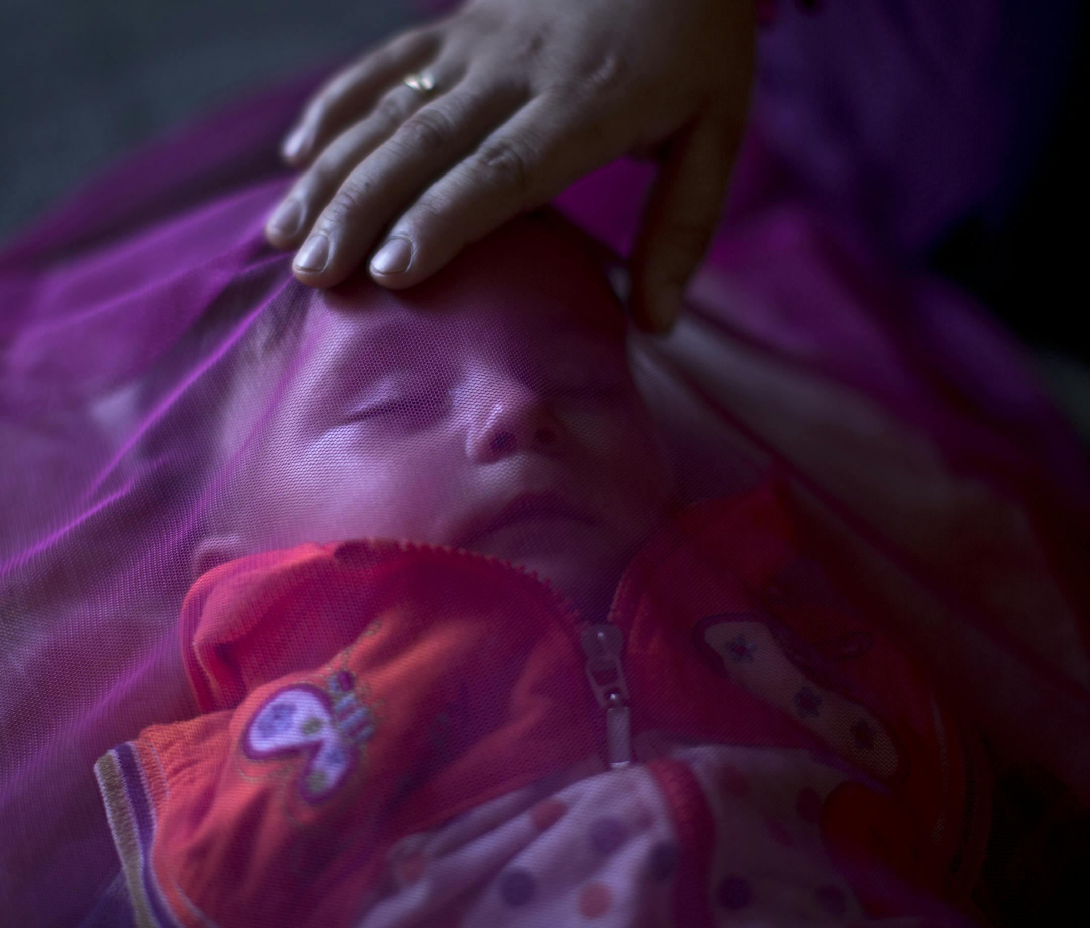 In this Tuesday, July 21, 2015 photo, Syrian refugee Kutana al-Hamadi, 24, tends to her son Almunzir, 7 months, covered with a mosquito net, whom she claims is suffering from malnutrition, at their tent in an informal tented settlement near the Syrian border on the outskirts of Mafraq, Jordan. "My son is too weak; my body doesn’t produce milk (and) ... we can’t afford buying milk,” says Kutana al-Hamadi. “We survived the barrel bombs in Syria but I’m afraid we