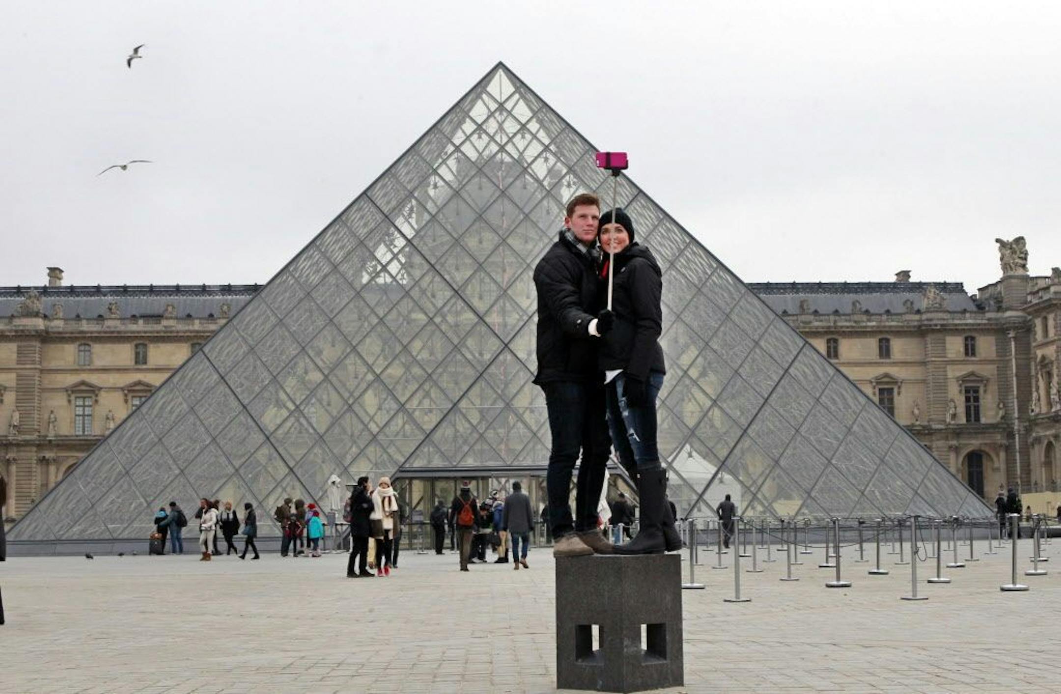 FILE - In this Tuesday, Jan. 6, 2015, Chris Baker and Jennifer Hinson from Nashville, Tennessee, use a selfie stick in front of the Louvre Pyramide in Paris. A French palace and a British museum have joined the growing list of global tourist attractions that have banned �selfie sticks� _ devices visitors use to improve snapshots, but which critics say are obnoxious and potentially dangerous. Officials at Chateau de Versailles outside Paris and Britain�s National Gallery in London announced the b
