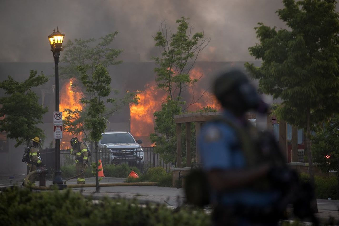 Firefighters battle flames at a business along University Avenue as riot officers police the street, Thursday, May 28, 2020 in St. Paul, Minn. Protests over the death of George Floyd, a black man who died in police custody, broke out in Minneapolis for a third straight night.