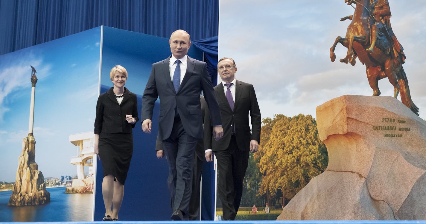 Russian President Vladimir Putin, center, arrives to attend a meeting with his supporters in Moscow, Russia, Tuesday, Jan. 30, 2018. Putin is expected to easily win another six-year term in this year's presidential election. A views of Crimea city Sevastopol is in on the left, St. Petersburg on the right. (AP Photo/Pavel Golovkin)