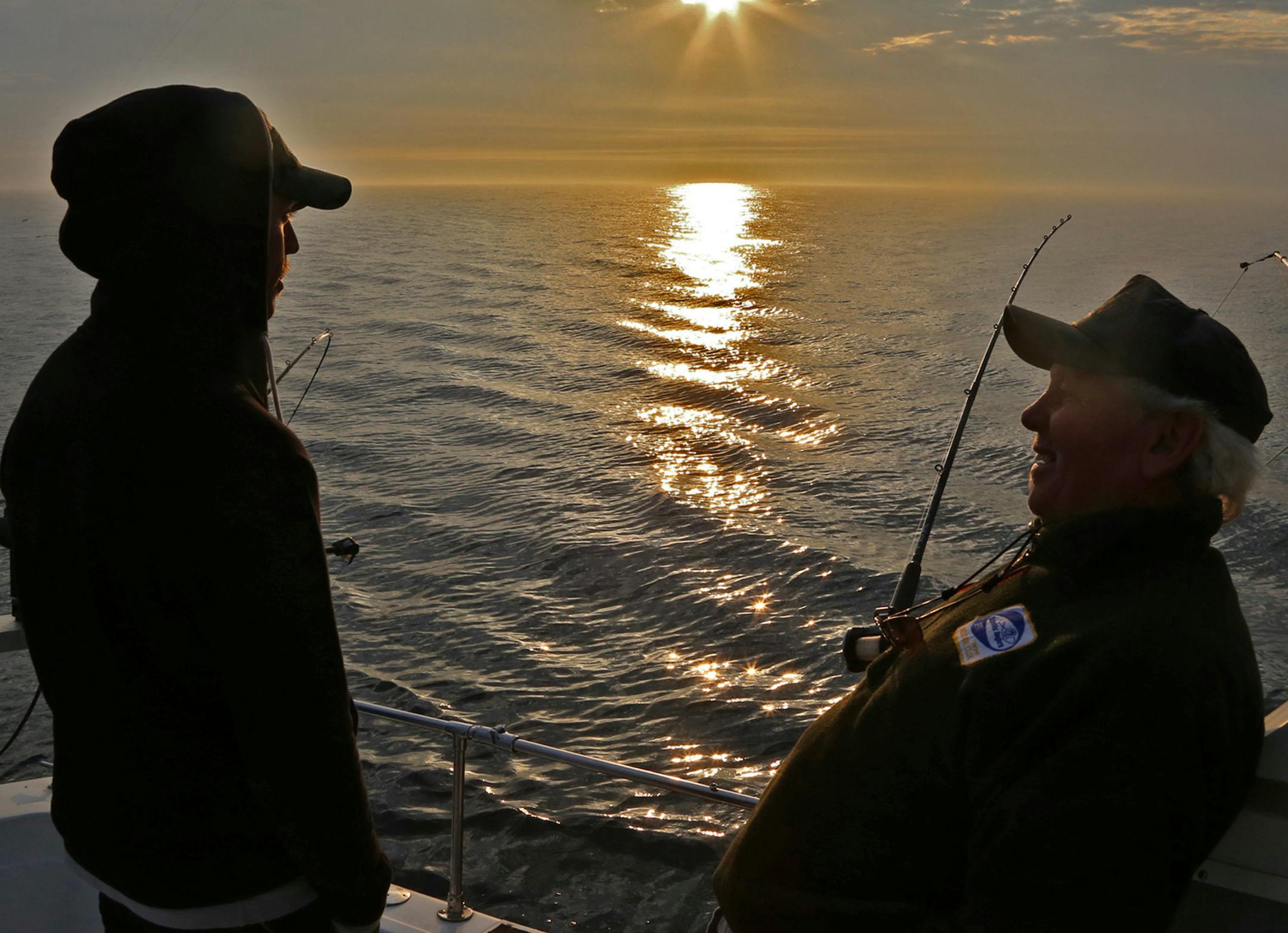 Bobby McGraw, left, and his grandfather, Bob Nasby, of the Twin Cities relax on Lake Michigan as the sun rises, waiting for salmon or trout to strike their lures.