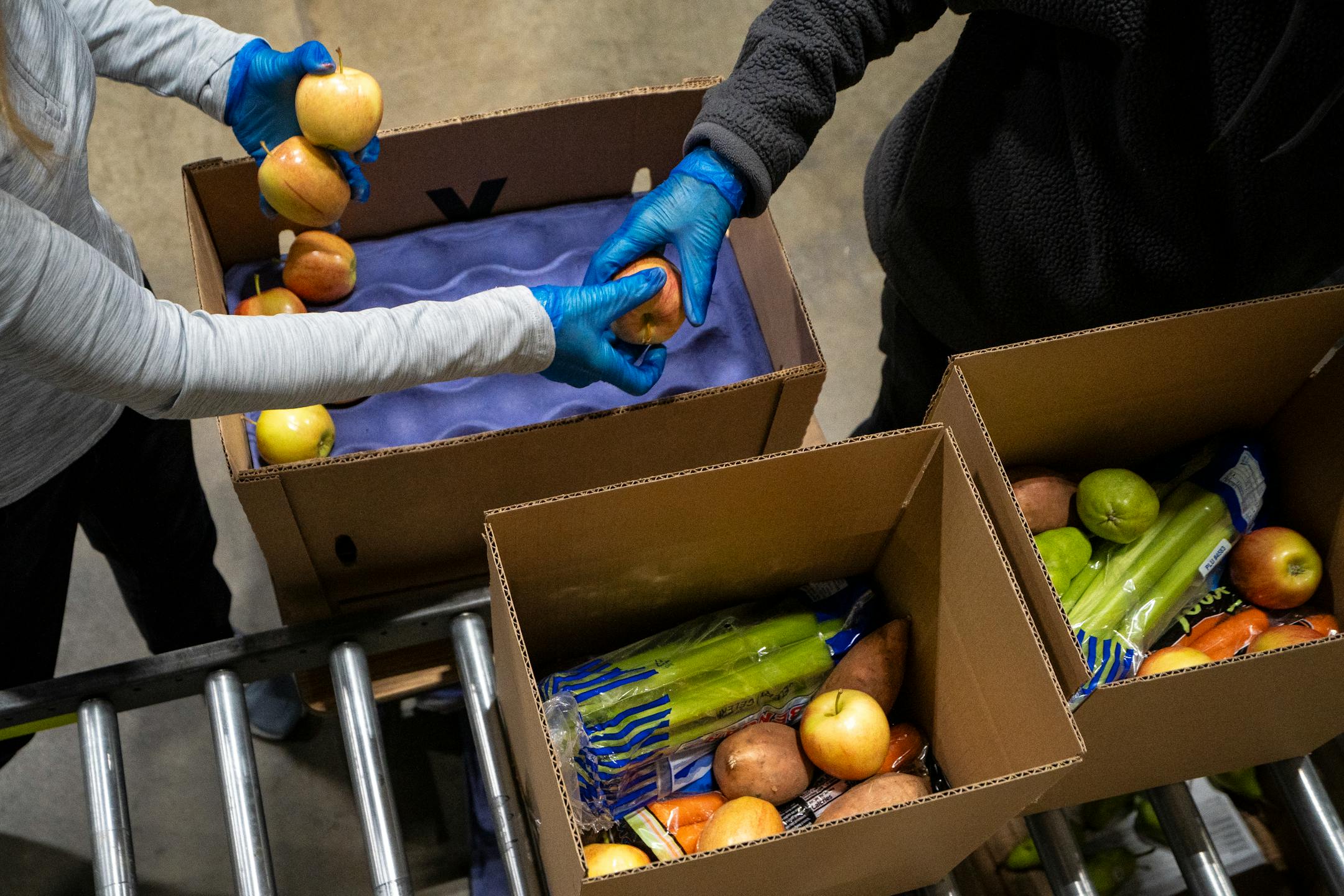 Lisa Merry and Trish Schaack, volunteers with the Food Group, pass apples to each other as they pack produce boxes during the food bank's "Pack to the Max" event.