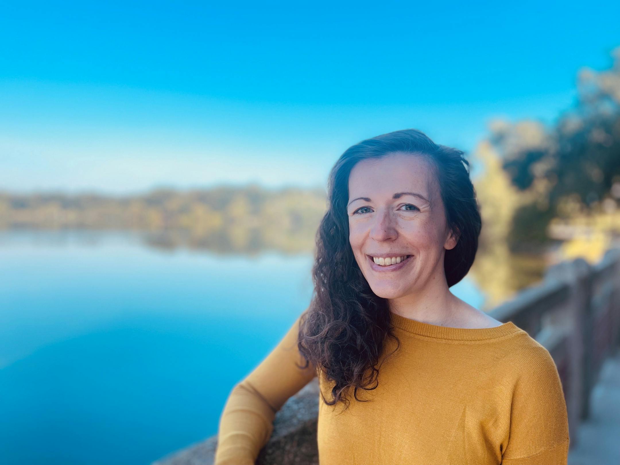 photo of author Claire Anderson-Wheeler, next to a body of water with trees in the background