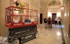 Historical painter Edward Peterson moves his scissor lift so workers can move a table down the hallway at the capital rotunda's east side Wednesday.