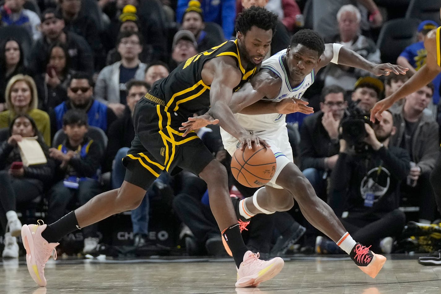 Golden State Warriors forward Andrew Wiggins, left, reaches for the ball next to Minnesota Timberwolves guard Anthony Edwards during the first half of an NBA basketball game in San Francisco, Sunday, Nov. 12, 2023. (AP Photo/Jeff Chiu)