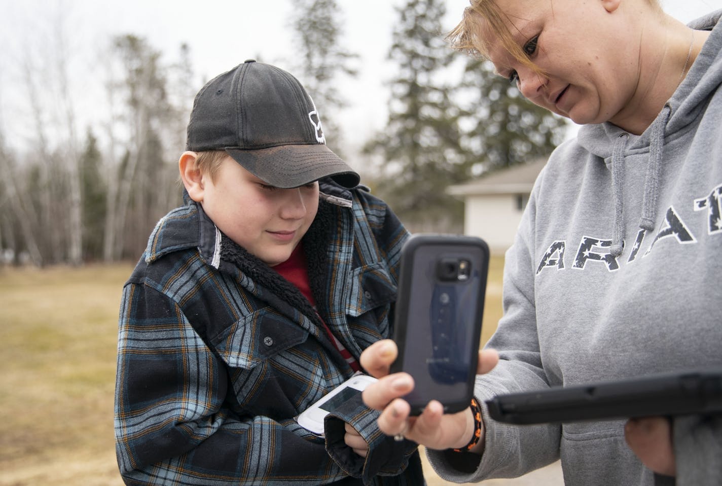 Tawnya Heino held up her son, Michael Zakrajshek's, phone so he could have a Zoom call with his teacher at the end of their driveway in Chisholm, Minn. They have to connect multiple times a day.