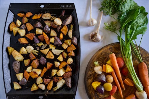 Turnips, carrots and potatoes on a platter before roasting alongside a pan with roasted chopped vegetables.