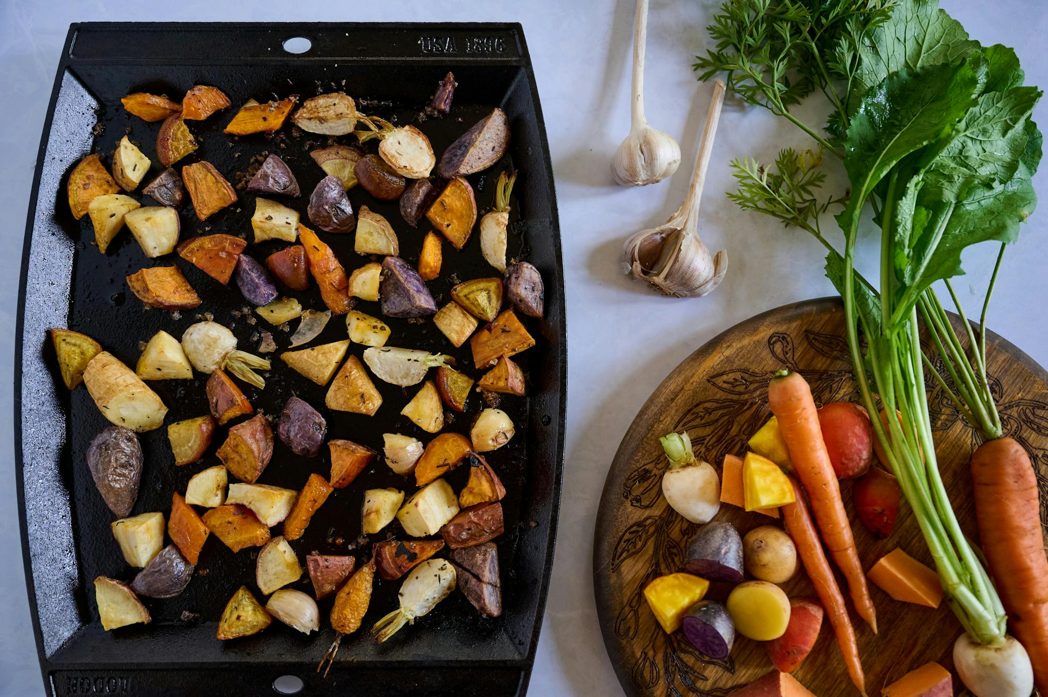 Turnips, carrots and potatoes on a platter before roasting alongside a pan with roasted chopped vegetables.