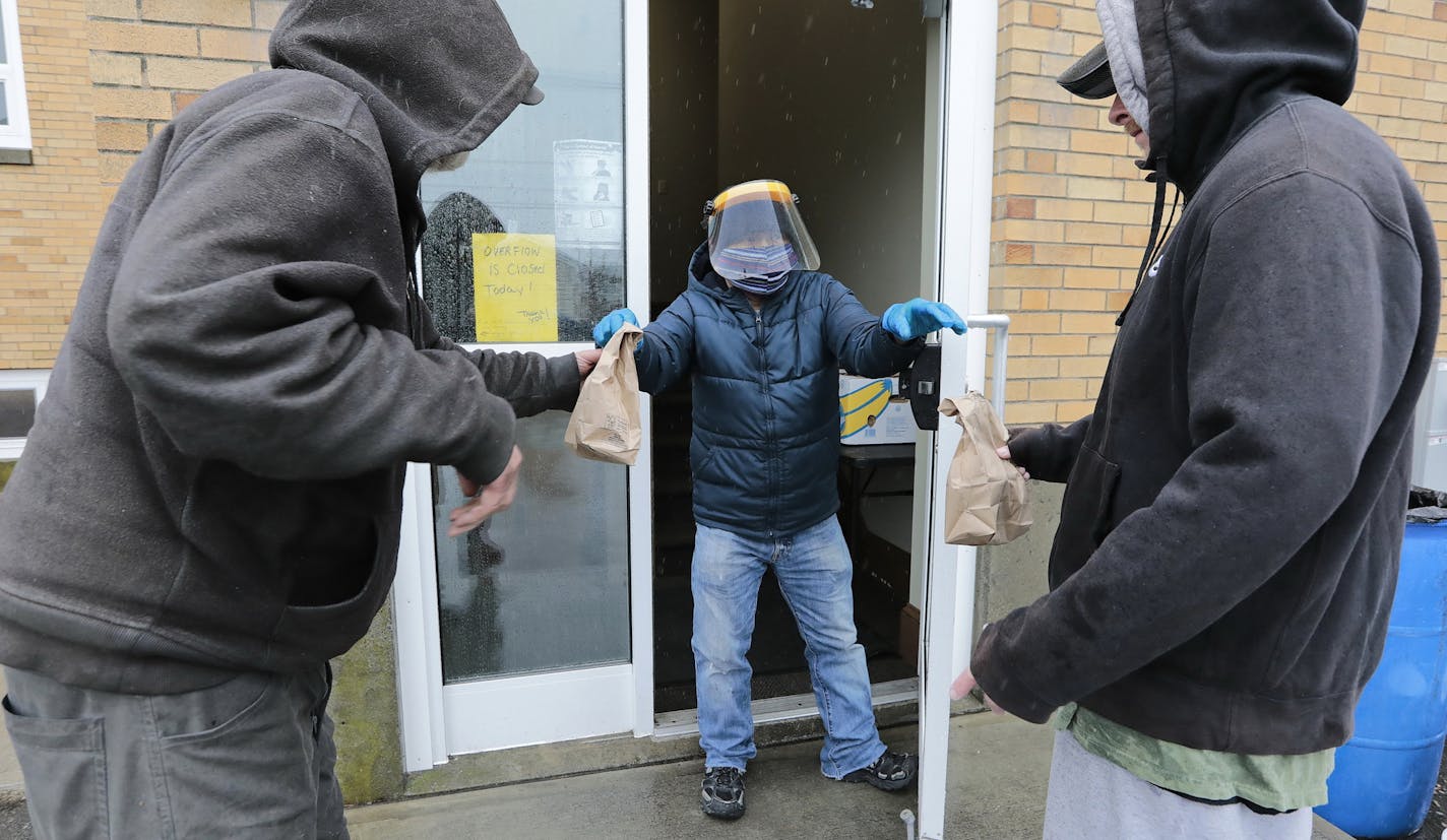 In light of the coronavirus pandemic, volunteer, Trung Dong uses a face mask and a shield, as he hands out meals to two homeless men at the Sister Rose House food pantry in New Bedford, Mass., on Thursday, March 19, 2020. The homeless are no longer allowed in the building and collect lunch at the door. (Peter Pereira/The Standard-Times via AP)