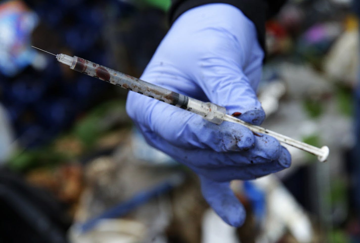 FILE - In this Nov. 8, 2017, file photo, Steph Gaspar, a volunteer outreach worker with The Hand Up Project, an addiction and homeless advocacy group, holds a used and blood-filled needle used for drug injection that she found while cleaning up a homeless encampment in Everett, Wash. Less than three months after President Donald Trump declared the U.S. opioid crisis a public health emergency in October 2017, the nation's governors are calling on his administration and Congress to provide more mo