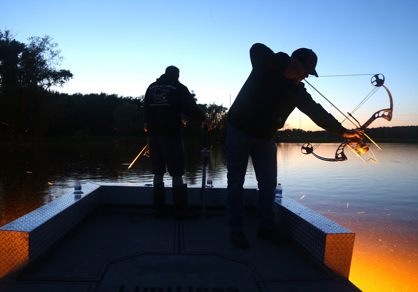 Patrick Kirschbaum,. right, of Rogers, draws back while bowfishing on Pool 2 of the MIssissippi River Wednesday night, drawing down on a dogfish. Carl Sassen, left, of Lino Lakes guides his custom bowfishing boat while looking in shallow water for carp, dogfish and other generally undesirables among finned species.