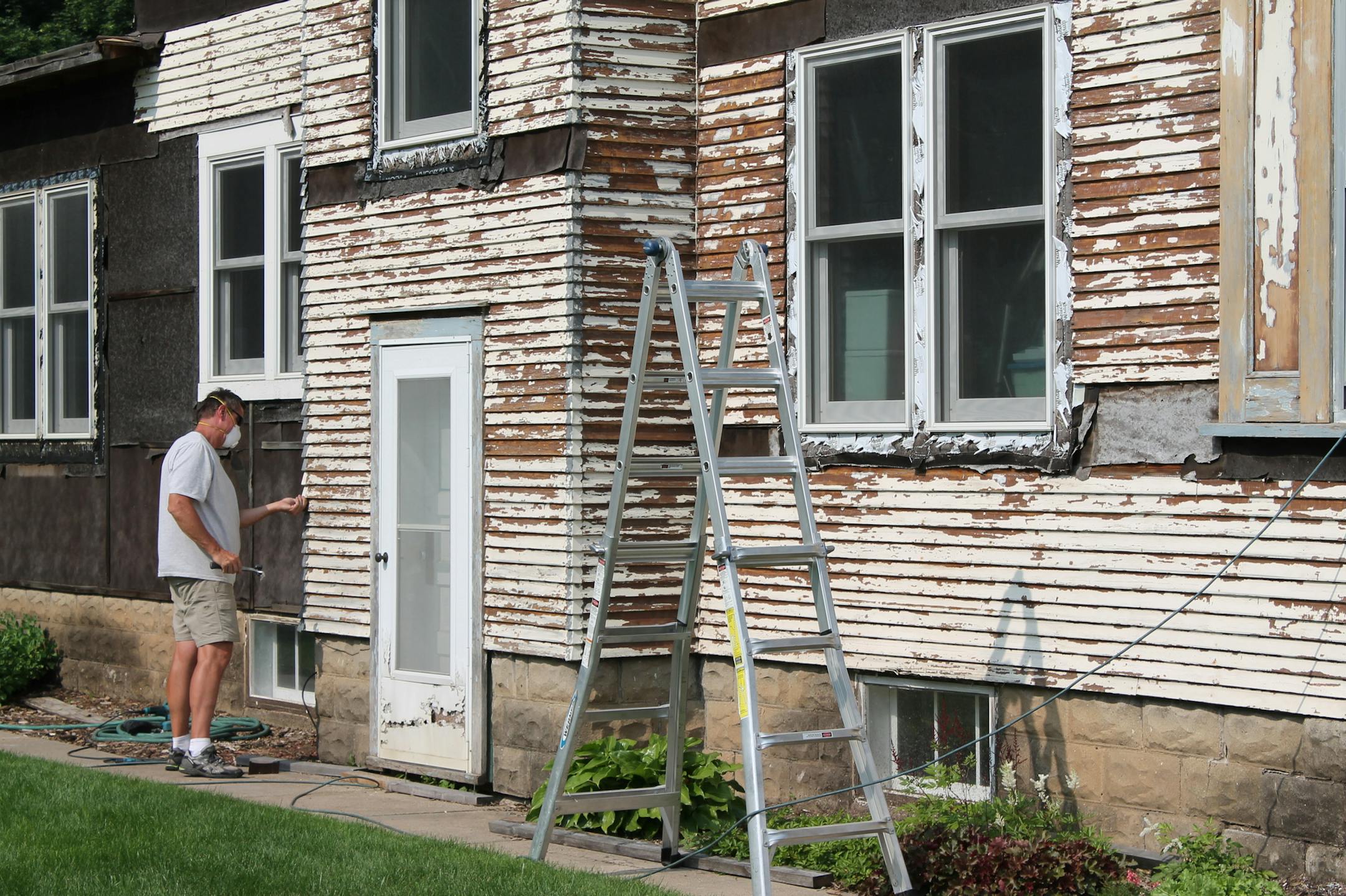 Lee Kindem, 54, scrapes old paint on siding of his girlfriend's house on a recent evening in Farmington. The city and neighborhood are calling the house on Spruce Street one of the worst cases of blight in town.