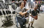 Chuck Aoki, a paralympic rugby player, helped Givenson Thimjon, 6, with shoulder pads during his shift at Dick&#x2019;s Sporting Goods