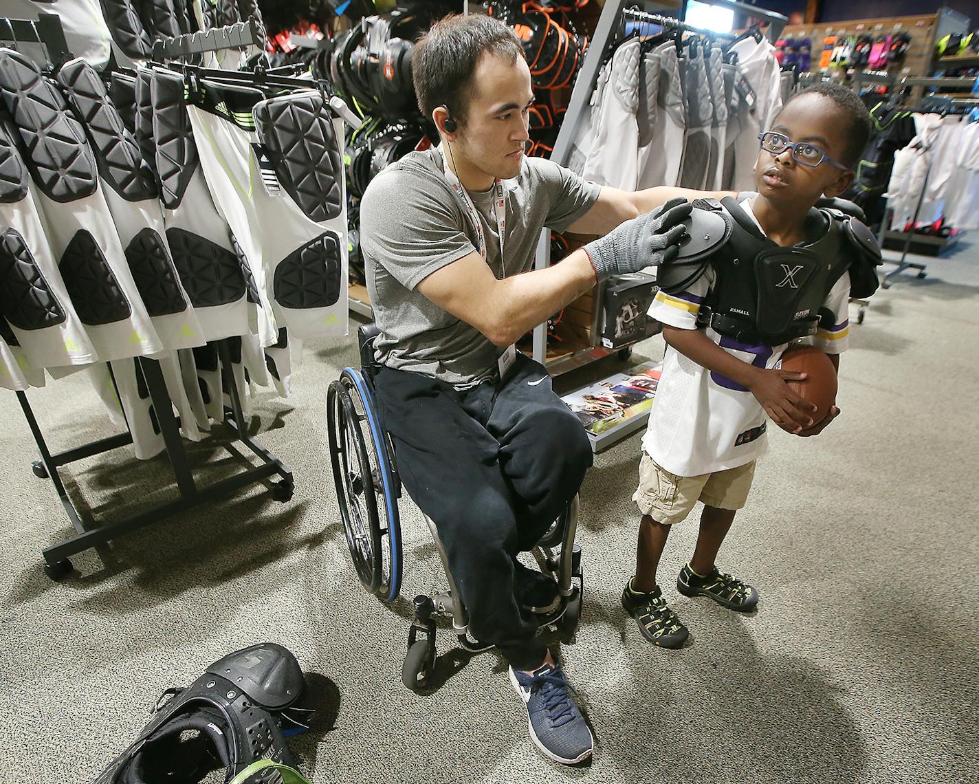 Chuck Aoki, a paralympic rugby player, helped Givenson Thimjon, 6, with shoulder pads during his shift at Dick&#x2019;s Sporting Goods