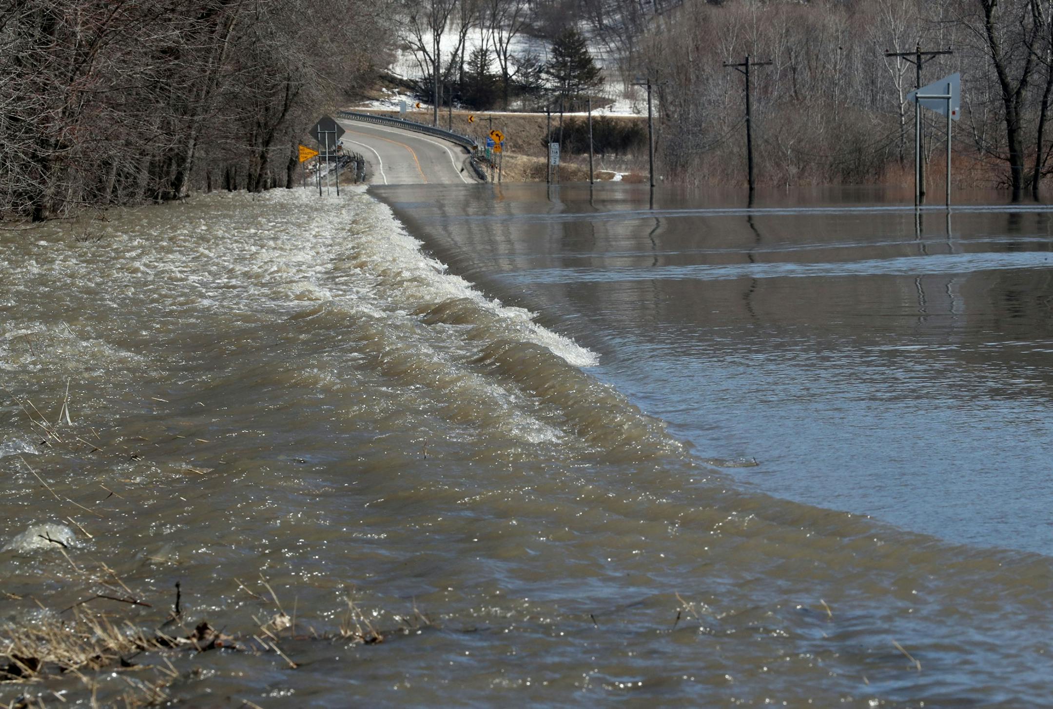 High water rushes over Highway 19 as melting snow along the Minnesota River is causing flooding and closing down three of four highways heading into town Wednesday, March 20, 2019, in Henderson, MN.